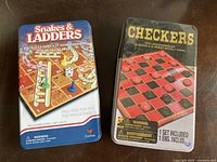 Closed tin boxes of Snakes & Ladders and Checkers games showing packaging and branding.