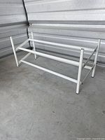 White metal adjustable extendable shoe rack shown assembled on concrete floor, displaying the horizontal bars and rubber feet.