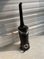 Full view of the black floor standing Air Innovations Clean Mist Smart Humidifier with tall narrow top outlet and power cord visible, placed against a metal surface.