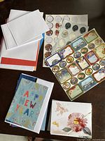 Greeting cards and envelopes laid out with two sheets of assorted stickers on a dark wooden surface.