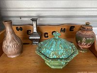 Set of four pottery items showing overall collection including three vases and one lidded dish on a wooden bench with welcome sign