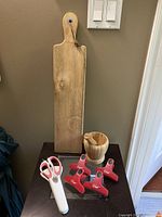 Wooden rectangular cheese board with handle and hanging loop, wooden mortar and pestle, white utility scissors with magnetic holder, and four red Master Chef magnetic clips sitting on black surface.