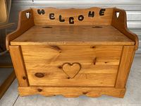 Front view of the wooden storage bench showing heart cutout and welcome sign on the back panel.