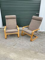 Two IKEA armchairs with brown fabric upholstery and light bent wood frames sitting outdoors on gravel against a green garage door.