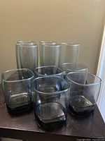 Front view of 5 tall and 5 short transparent smoke glass drinking glasses arranged in two rows on a dark wooden surface.