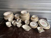 Overall view of set showing stacks of plates, bowls, cups, saucers, and gravy boats with white, floral and gold design.