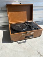 Record player in open brown and black suitcase-style case showing turntable and controls.