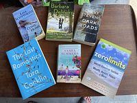 Top view of the six paperback books arranged on a wooden table showing front covers.