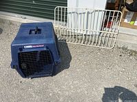 Blue Pet Mate Deluxe Vari Kennel dog crate with metal gate in outdoor setting, showing crate and gate separated.