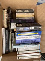 Full view of multiple fiction books packed in a cardboard box showing various titles and conditions