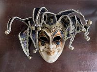 Full view of the handcrafted Italian Venetian jester mask with fabric points, bells, and lion embellishment on the forehead.