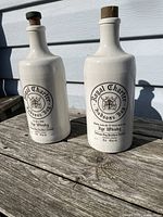 Front view of two white ceramic whiskey bottles on outdoor wooden surface showing Royal Charter Hudson's Bay branding.