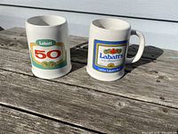 Photo showing front view of two ceramic beer mugs with Labatt's Beer emblems, placed on wooden surface.