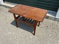 Front angled view of wooden Mid-Century Modern style coffee table with visible surface wear and slatted shelf underneath.