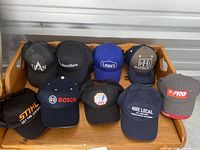 Tray of eight adjustable strap cotton blend hats in various colors and branded logos.