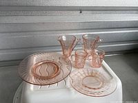 Overall view of different sizes and styles of pink Depression glass plates and cups with handles.