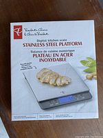 Photo showing the front of the product box with branding, an image of the digital kitchen scale on the front showing sliced food on the platform and digital display reading.