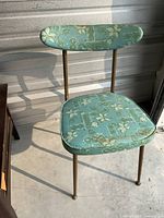 Front view of retro turquoise chair showing metal legs and vinyl upholstery with gold pattern
