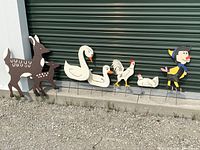 Full set of 5 rustic wooden garden stakes featuring a deer pair, swans and duck, rooster and chicken, and a colorful unique character against a green garage door.