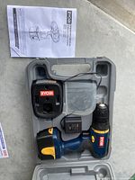 Empty hard plastic molded Ryobi case holding cordless drill, charger, manual, and battery in spots designed for each.