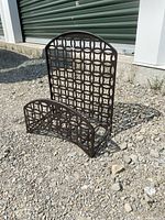 Front and side view of the brown metal hose rack with geometric circular design and arched top placed outdoors on gravel.