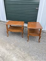 Two traditional wooden side tables with cabriole legs, brown finish, visible surface wear, placed outdoors in front of a storage door.
