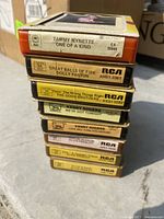 Stacked 8-track tapes showing titles and artists including Tammy Wynette, Dolly Parton, The Good Brothers, Kenny Rogers, Elvis Presley.
