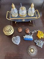 Full view of all items: salt and pepper shakers set with mustard pot on metal tray, brass heart-shaped box, brass item with holes, two walnut shell objects, two keychains, and metal floral decorations.