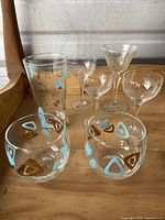 Photo showing full set of 7 vintage glassware pieces on wooden surface, including glasses with retro blue and brown geometric patterns and clear etched stemmed glasses.