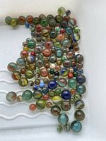 Full spread of approximately 70 glass marbles showing various sizes and mixed swirl and solid color patterns in a white container.
