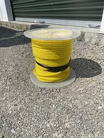 Side view of the yellow polypropylene rope tightly wound on a clear plastic spool sitting on gravel outside a storage unit.