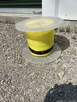Side view of bright yellow polypropylene rope wound around clear plastic spool on gravel surface.