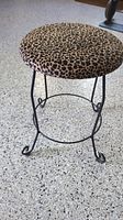 Side angle of round animal print vanity stool showing seat pattern and metal curled legs.