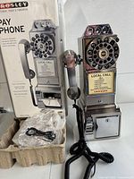Front view of the Crosley 1957 style payphone replica showing chrome finish, rotary-style dial with push-button operation, coin slots, handset, and original packaging.