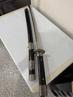 Full view of katana sword laid next to open scabbard showing curved blade and fittings.