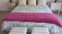 Bed made with bed runner draped over foot of bed showing solid pink side facing up.