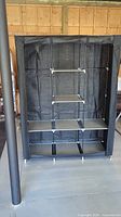Front view of the large black fabric portable closet with shelves visible inside and open flap.