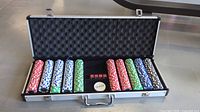 Open poker set showing multiple stacks of poker chips in various colors, five red dice, and a dealer button inside a foam-padded aluminum case.