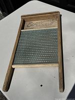Front view of vintage Economy glass washboard on white surface, showing wood frame and detailed textured glass panel with 'Economy Glass' printed at top.