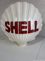 front view of white shell-shaped milk glass globe with raised red SHELL lettering