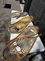 Top view of three pairs of vintage wooden snowshoes placed on a white table outdoors, showing shapes, sizes and woven bindings.