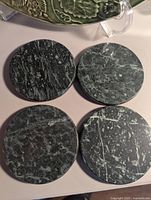 Four round green marble coasters arranged in a square pattern, showing their polished surfaces with natural white veining.