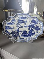 Front view of blue and white porcelain platter with Chinoiserie landscape design on a display stand.