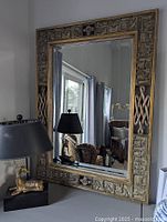 Large rectangular gilt and carved mahogany framed mirror shown on table next to black lamp and gold deer figurine, revealing detailed carving and distressed finish.