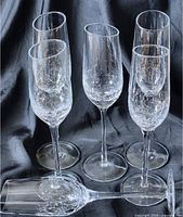 Four crackle crackle glass champagne flutes upright and one lying down on black fabric background, showing slanted rims and crackled texture