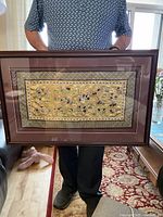 Full view of the framed tapestry held up by a person showing dimensions and overall condition