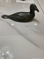 View from the side showing dark stone bird carving with smooth polished finish and carved feather details.