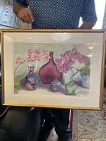 Full view of framed watercolor painting depicting orchids in vases against a muted background under glass with gold frame.