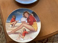 Front side of the collectible plate showing artistic illustrations of Norma Jeane in various poses on a beach with a volleyball.