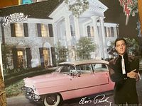 Poster showing Elvis Presley with Graceland mansion and a pink vintage car at night.